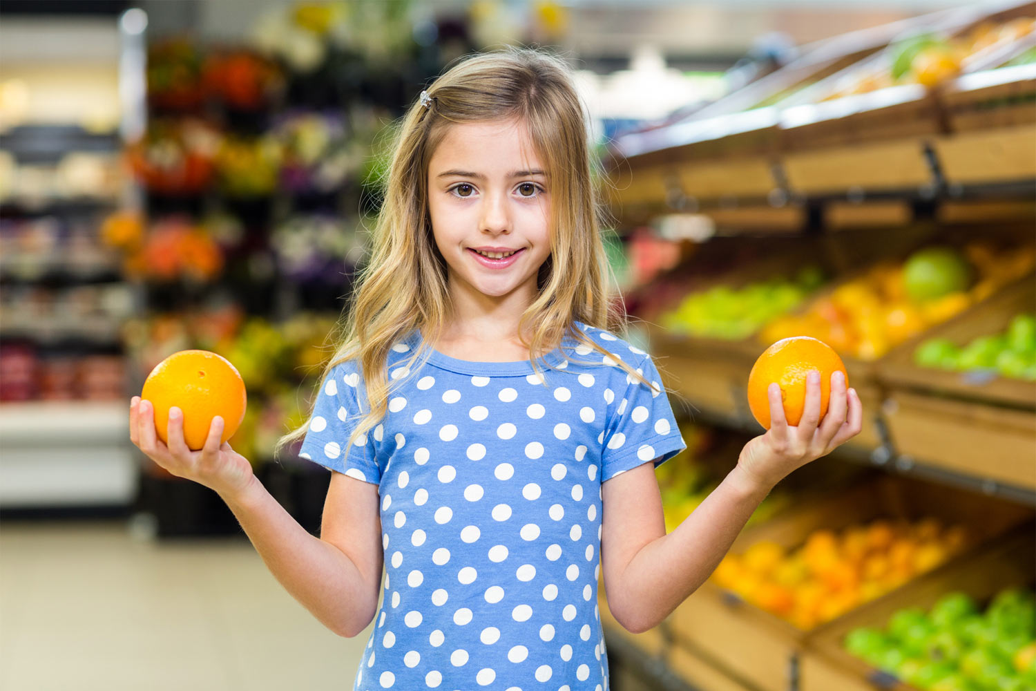 little girl in store holding two oranges