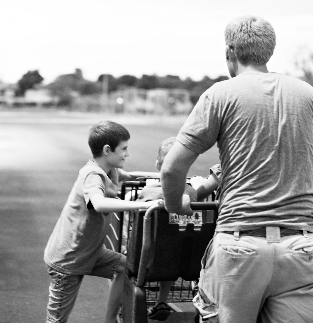 Black and white photo of a dad and son on a walk and pushing a cart with an infant in the baby seat