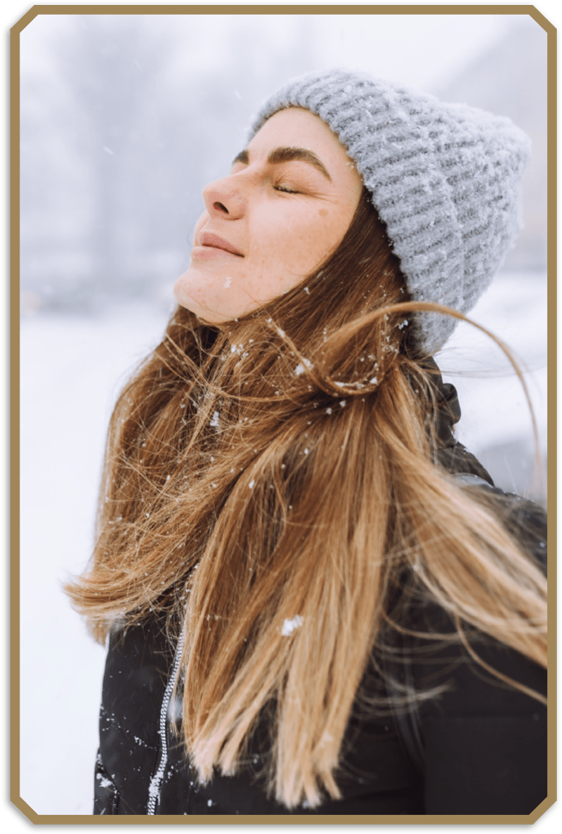 young girl standing in the snow wearing a beanie serenely lift her face towards the sky with her eyes closed