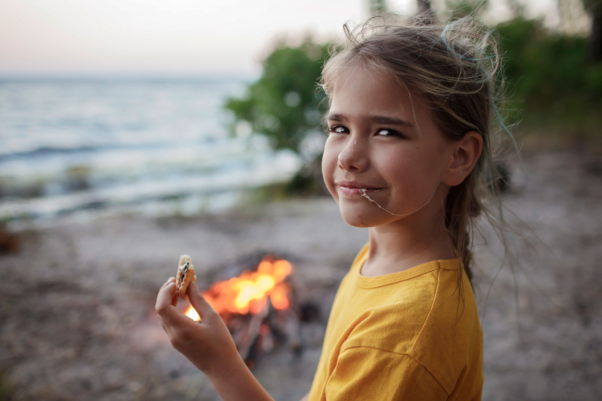 Girl eating a s'more in front of a campfire