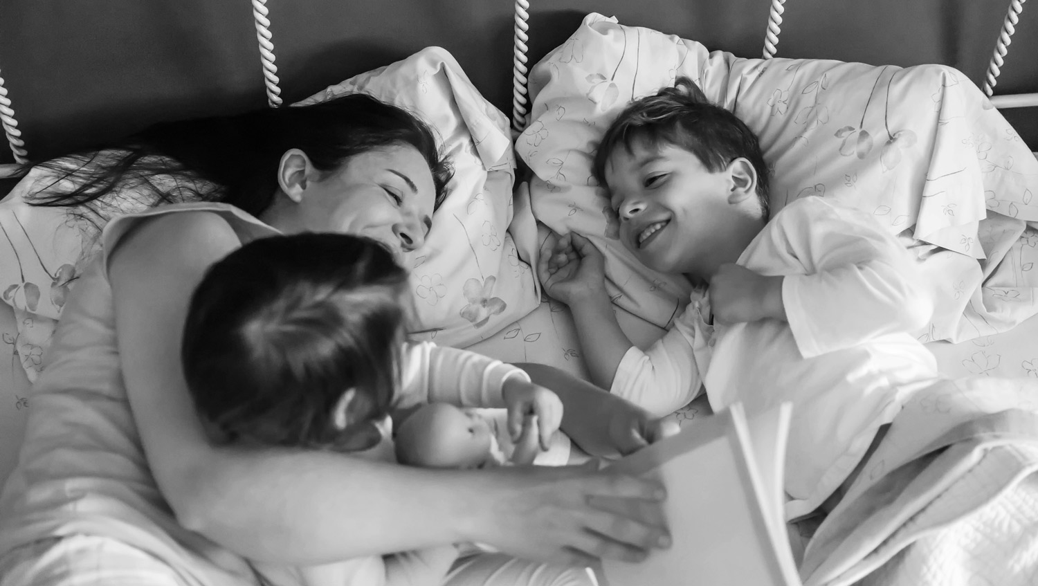 mother reading a book to two of her kids in bed