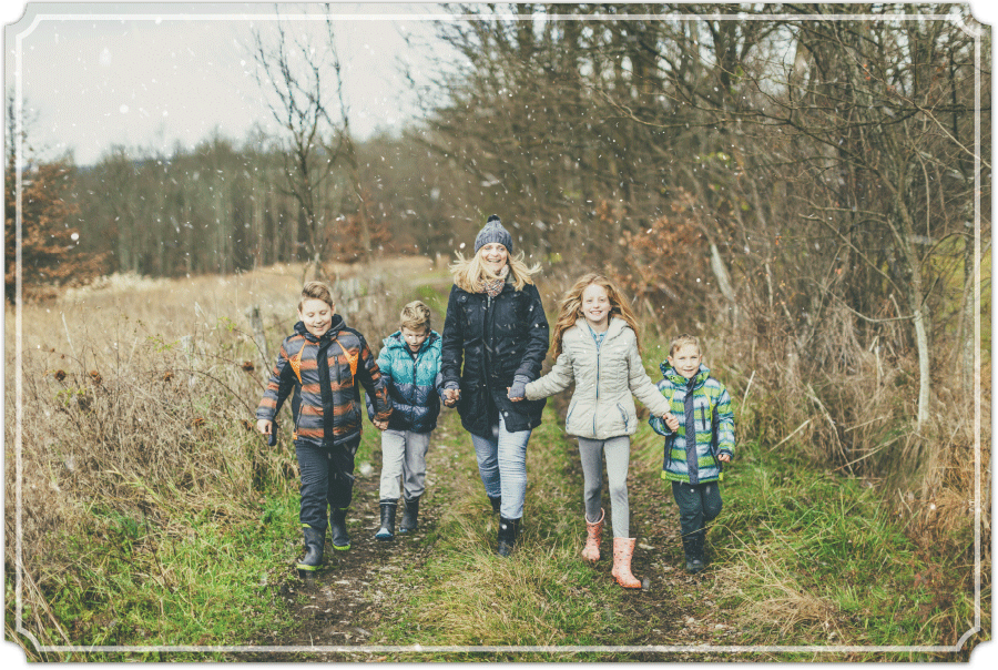 Family walking towards the camera, in a backdrop of fields and forests during a light snow