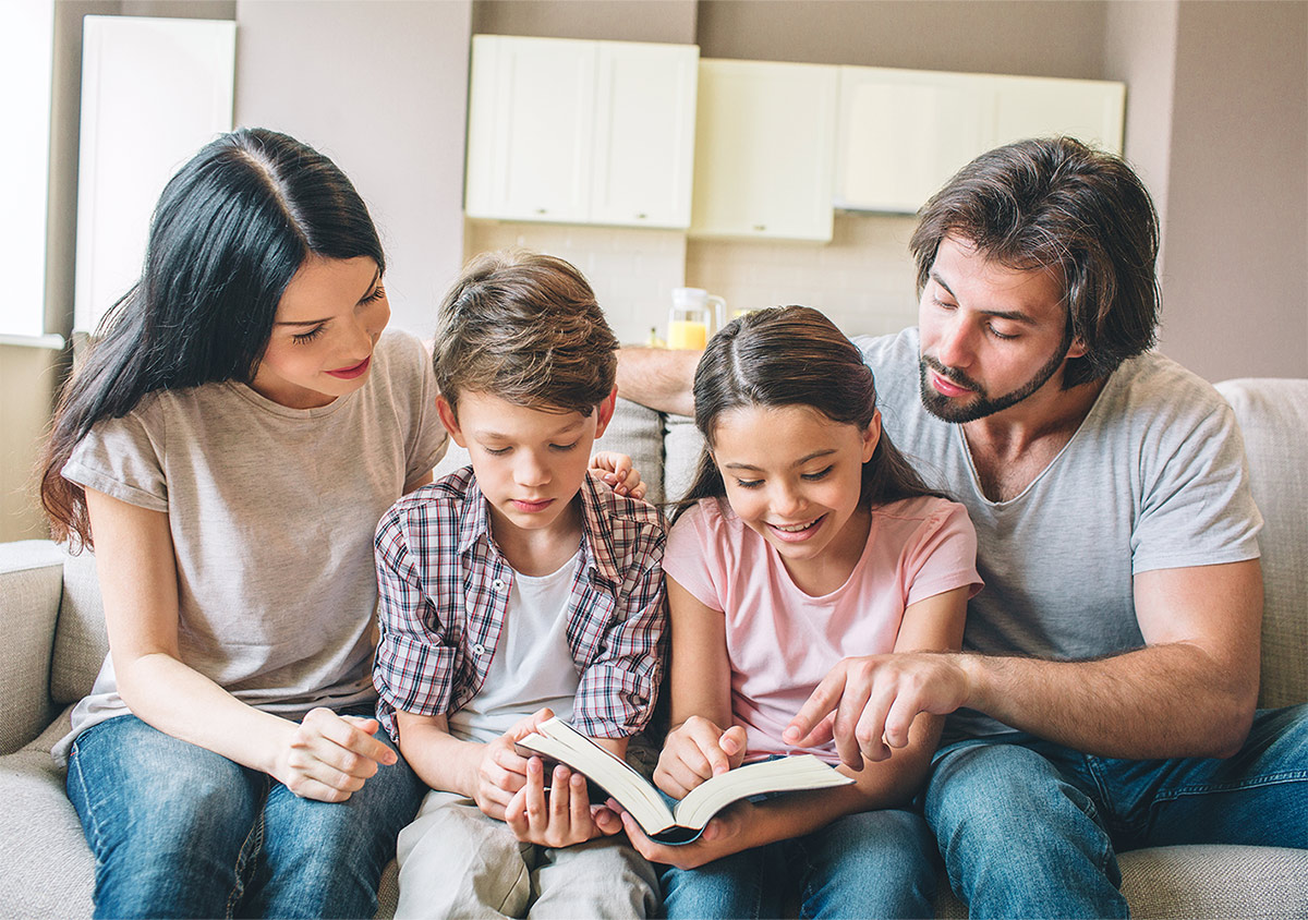 family of mother, father, son, and daughter looking at book