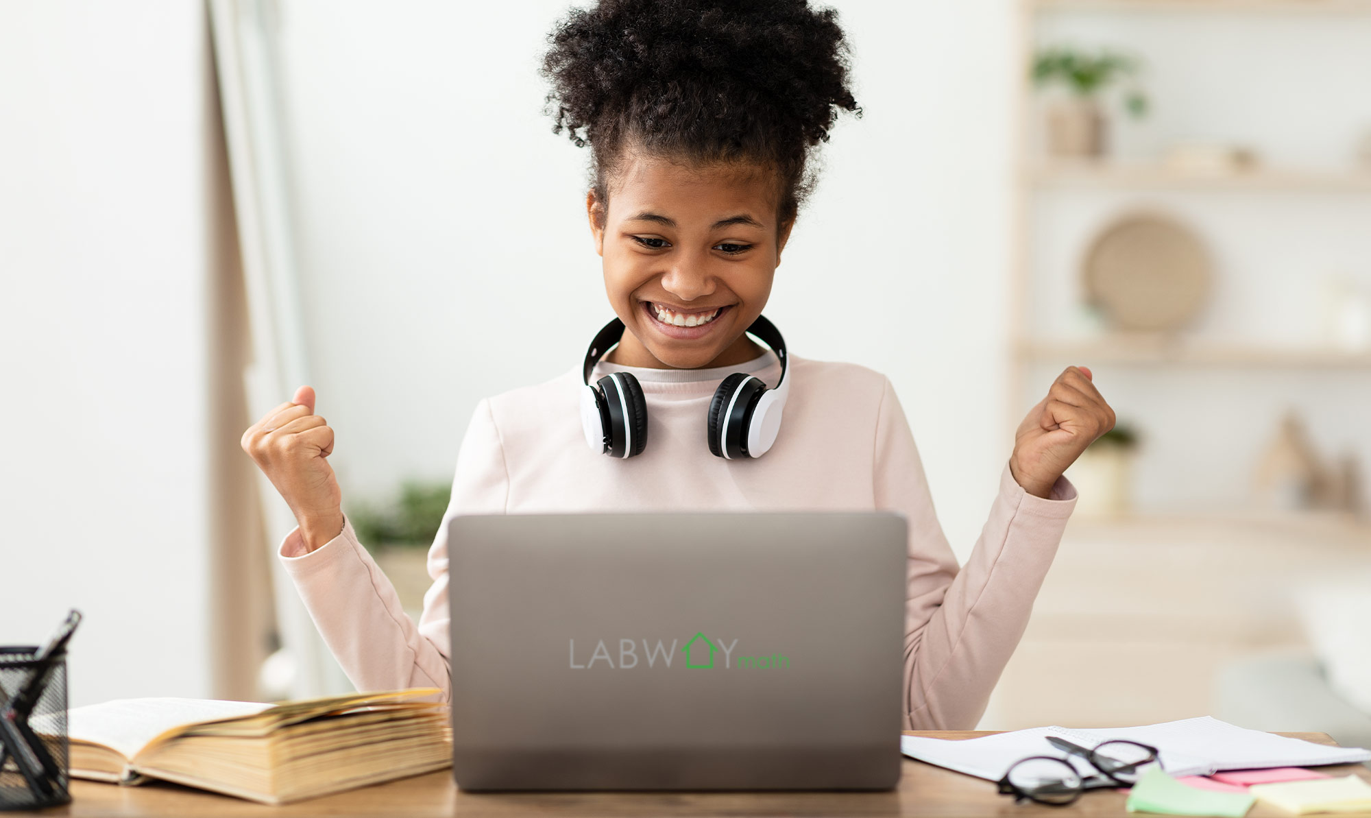 a young girl wearing headphones around her neck and an excited look on her face sits at a laptop with the the LABWAYmath logo on the back of the display screen