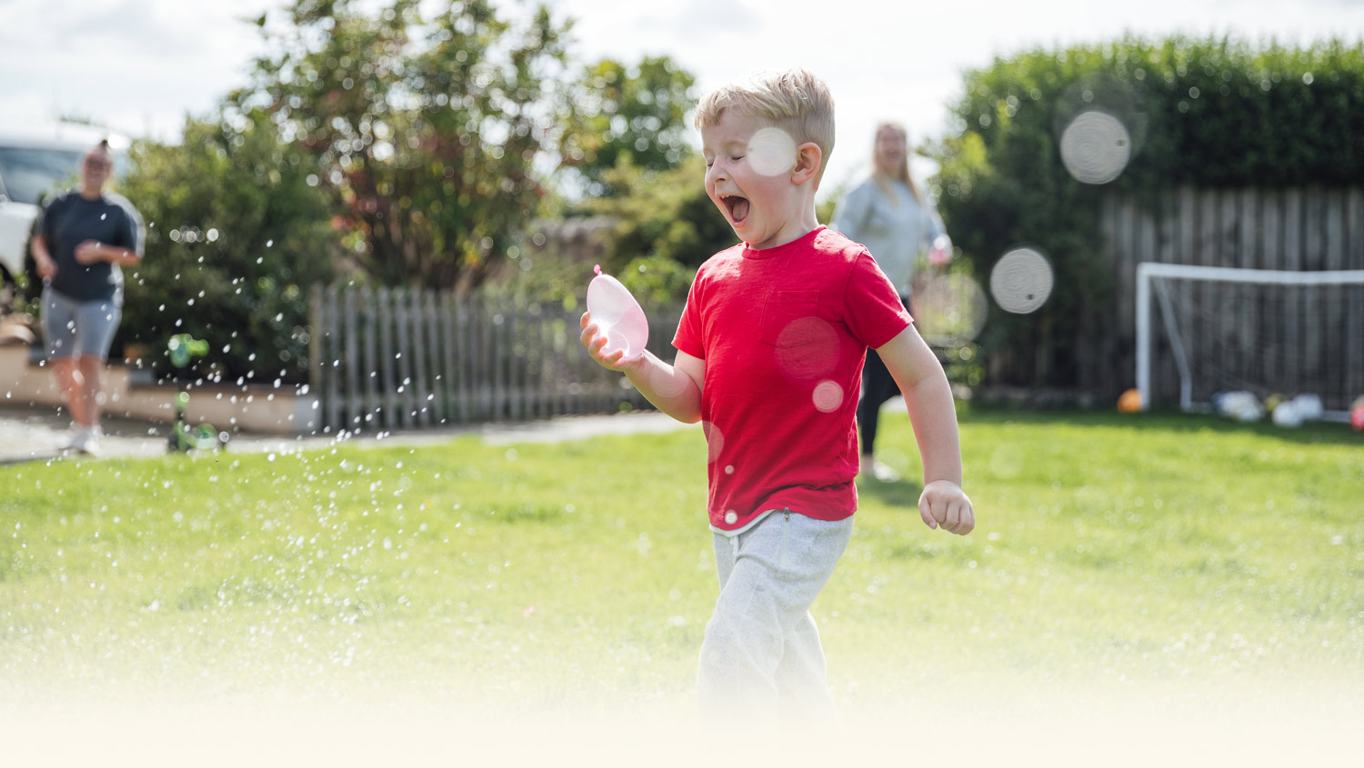 young child wearing red tshirt holding water balloon and laughing