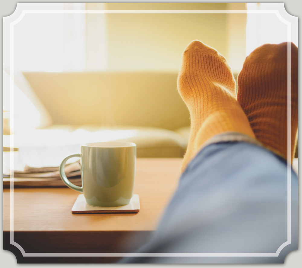 legs with feet on the coffee table with socks on next to a coffee mug on a coaster