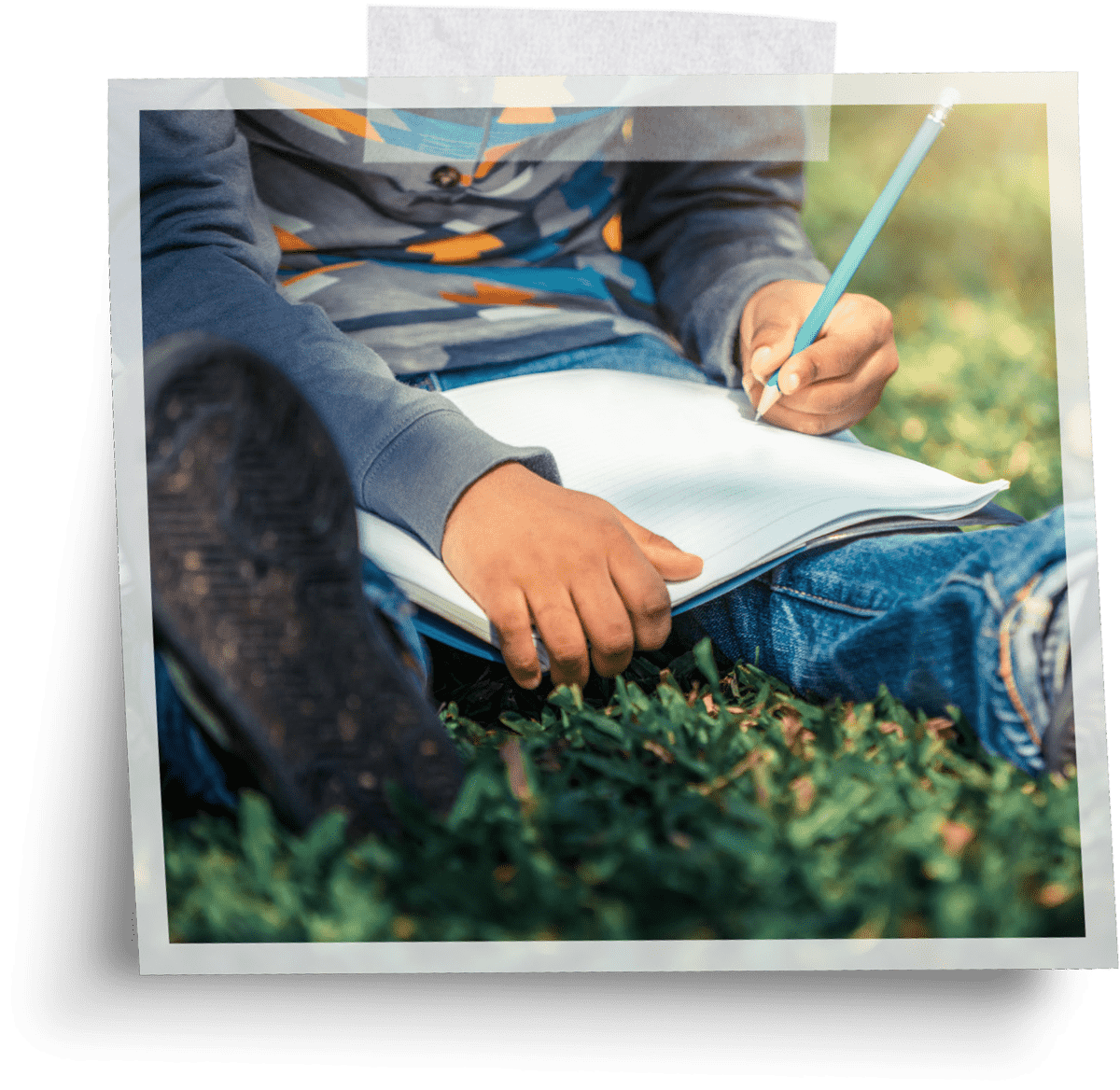 cropped view of a child sitting on grass and writing in a notebook