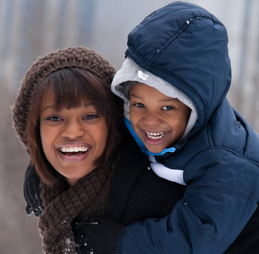 Woman holding young boy on her back while smiling in snowy setting