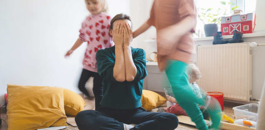 mom covering her eyes while on the floor while her children run around her