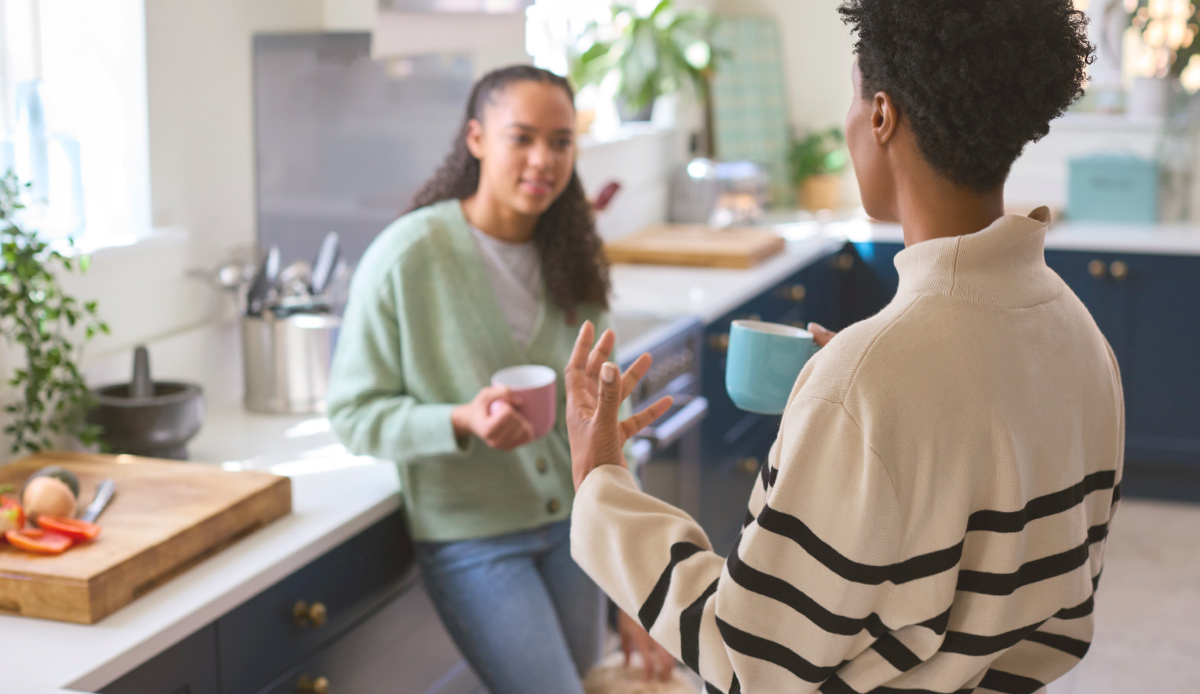 parent talking to daughter in kitchen while holding mugs