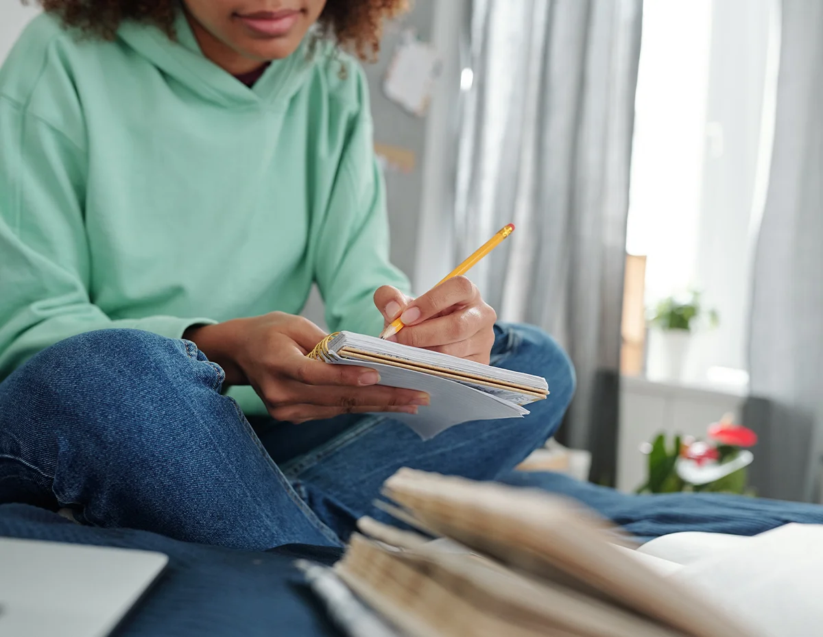 person sitting on the floor and writing in a notebook