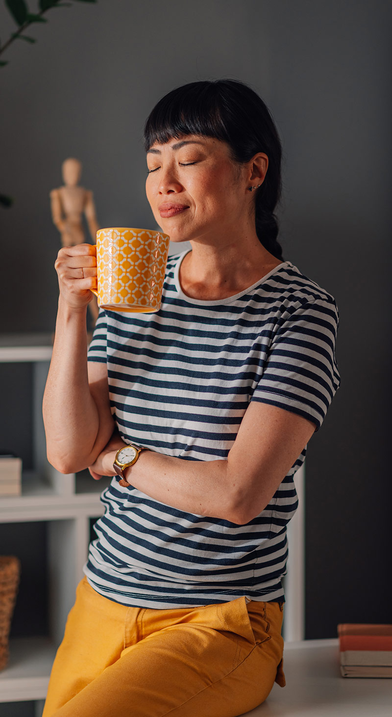 a woman leans on a table holding a mug and closing her eyes in a moment of internal thought