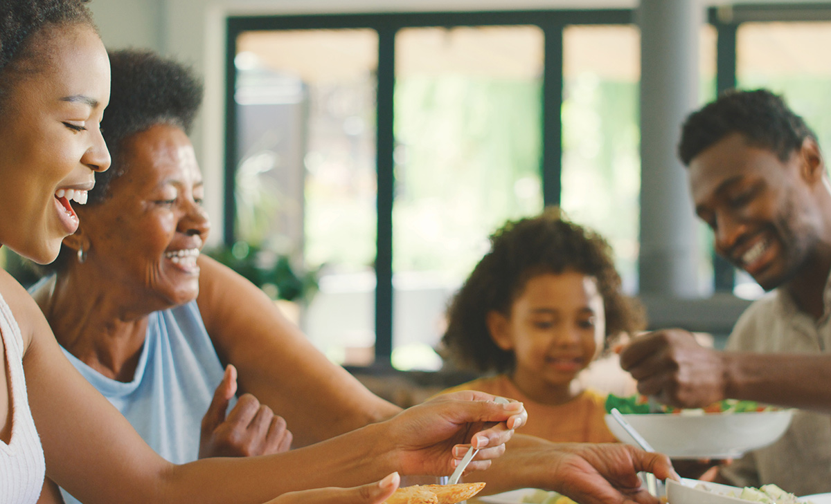 family at dinner table smiling while eating and passing bowls