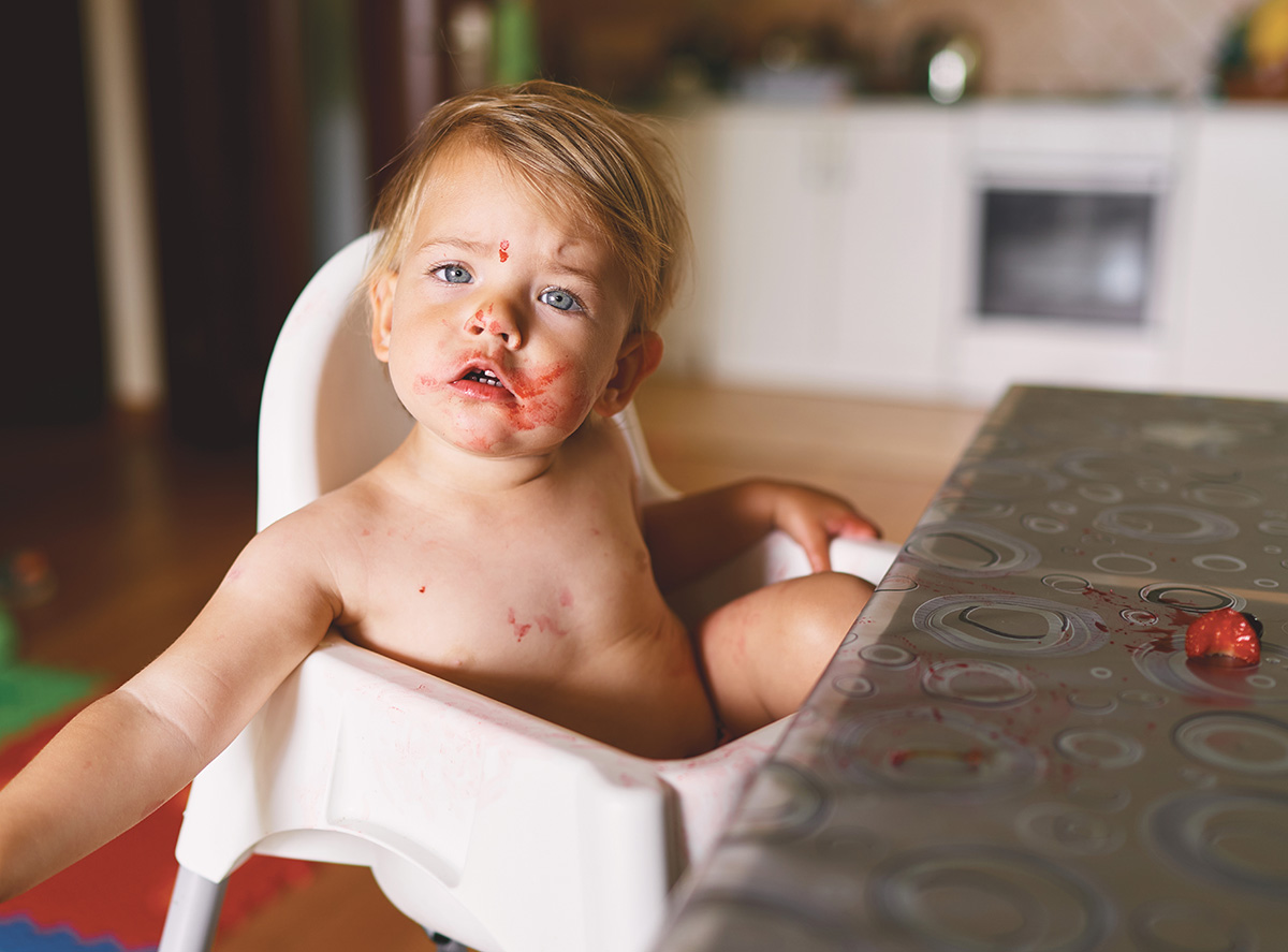 A toddler sits in a high chair with a messy face after eating.